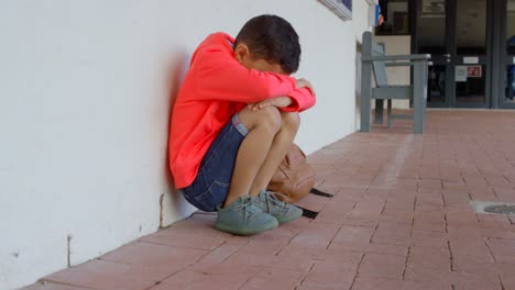 Side-view-of-Asian-schoolboy-with-head-down-sitting-alone-on-the-floor-in-corridor-at-school-4k