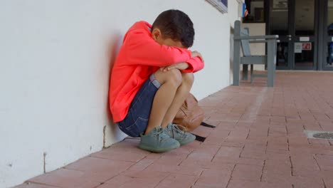 side view of asian schoolboy with head down sitting alone on the floor in corridor at school 4k