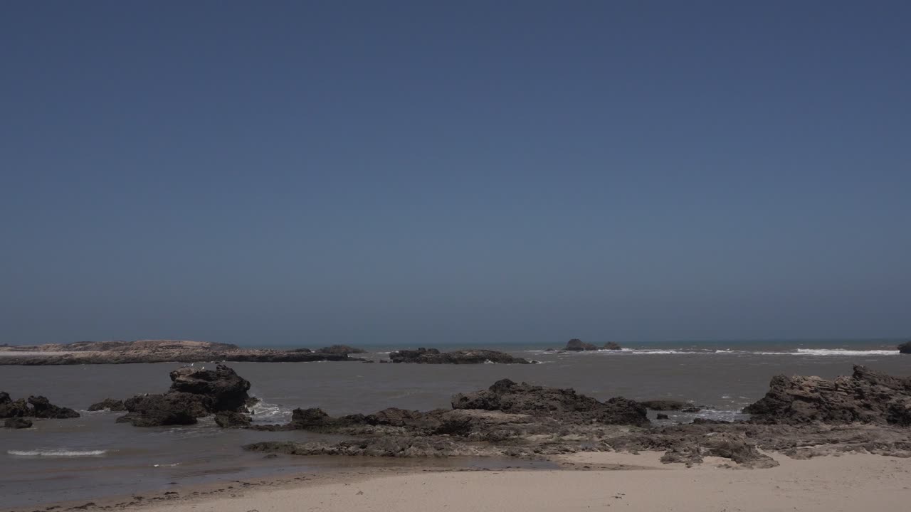 You see many clusters of rocks along the seashore. The sky is bluish and beautifully clear