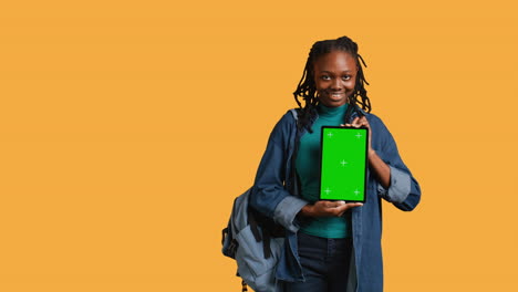 Smiling-woman-presenting-tablet-with-green-screen-display,-studio-background