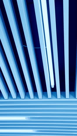 walking under the plank ceiling with long led lamps. switched on white light illumination. view from below. vertical video