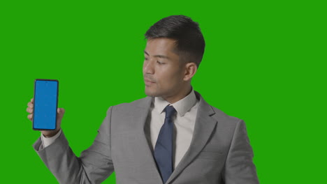 studio shot of businessman in suit holding blue screen mobile phone against green screen