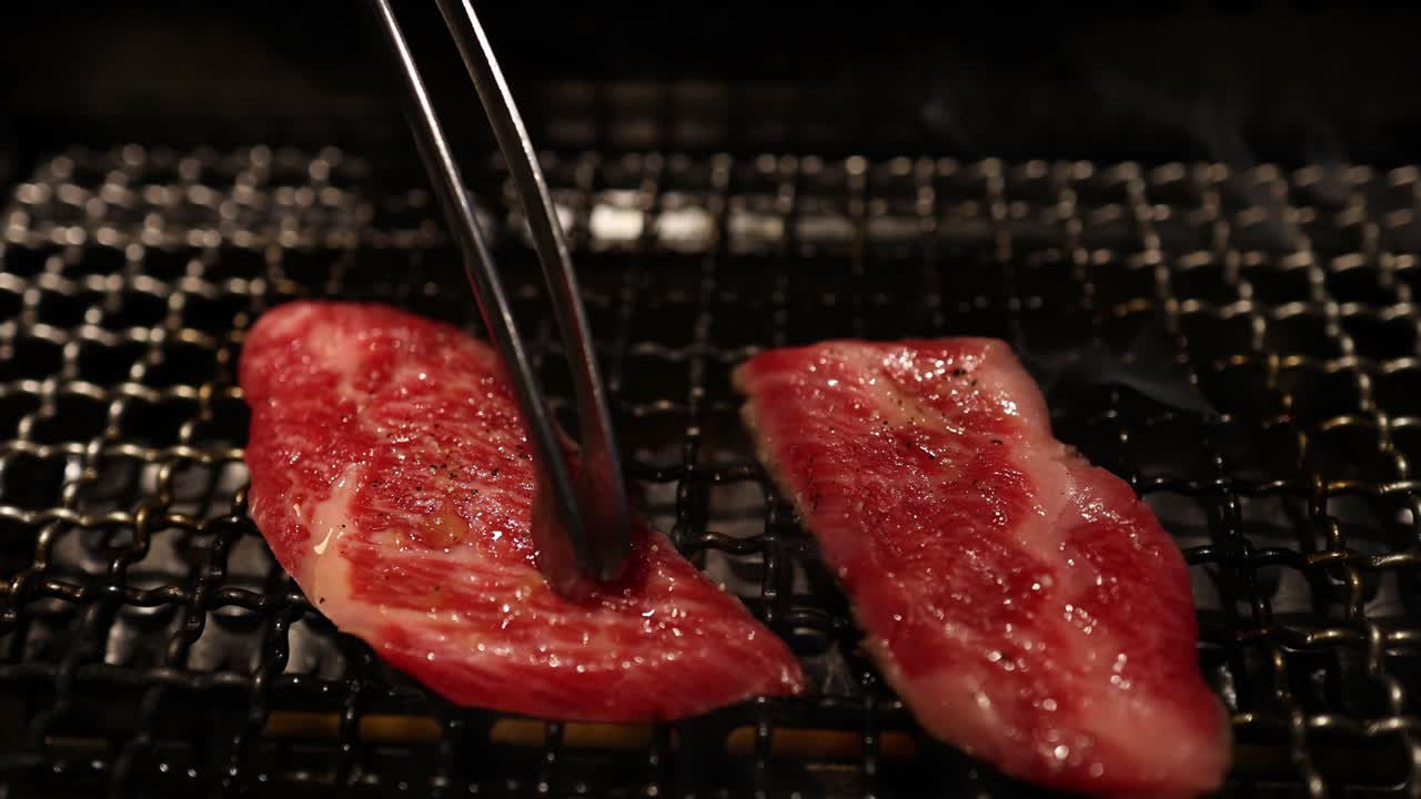 Steak grilling on a hot metal grate with tongs