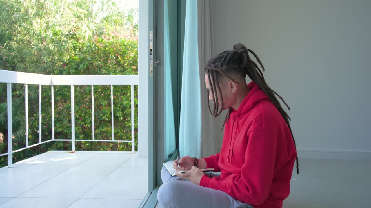 Uomo afroamericano che apre le tende, poi si siede sul balcone scrivendo idee in un quaderno, spazio per il testo.