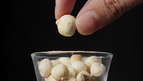 a hand picks a piece of white cardamom dried seed pod in glass bowl