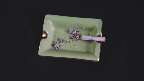 smoking and ashing a rolled cigarette or joint, legalised marijuana on green ashtray