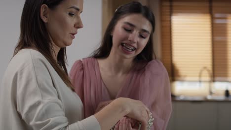 zoom out of caucasian woman applying flower corsage on girl's wrist before prom