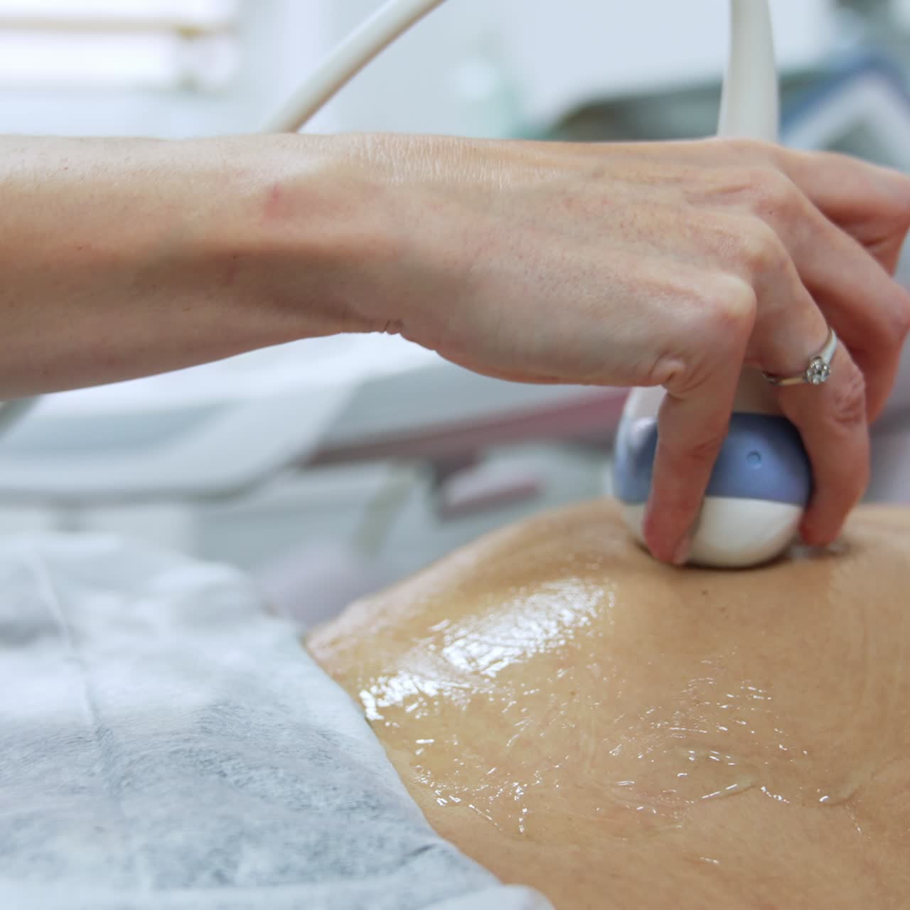 Pregnancy examination at ultrasonic equipment. Obstetrician moving the device by the little rounded belly of woman