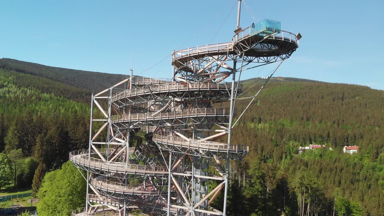 Aerial elevation tilt-down shot of the man standing on the platform of the sky walk observation tower in Sudety mountains