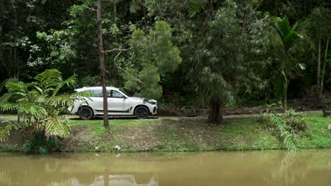 kuala lumpur, malaysia - march 9, 2022: brand new car 2020 bmw x5 wheelhouse interior. concept of luxury. hybrid cars. white bmw x5 suv driving down the road with a river in the foreground.