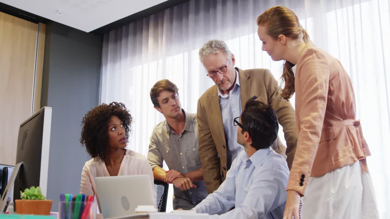 Businessman and coworkers discussing over laptop at desk