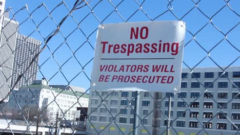 no trespassing sign on fence with buildings in the background