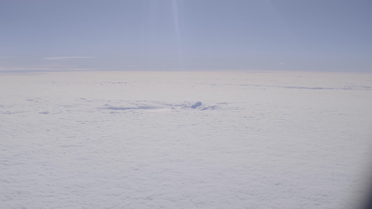 Clouds with mountain peaks faintly visible under bright daylight, aerial view