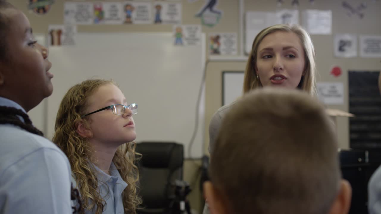 Young teacher smiles and answers questions with diverse class of students