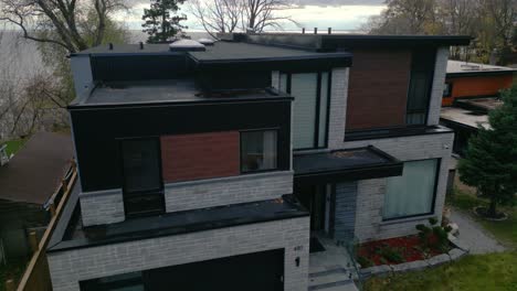 drone ascends tilting down on luxurious suburban house with large windows and minimalistic modern design aesthetics, black and grey accents