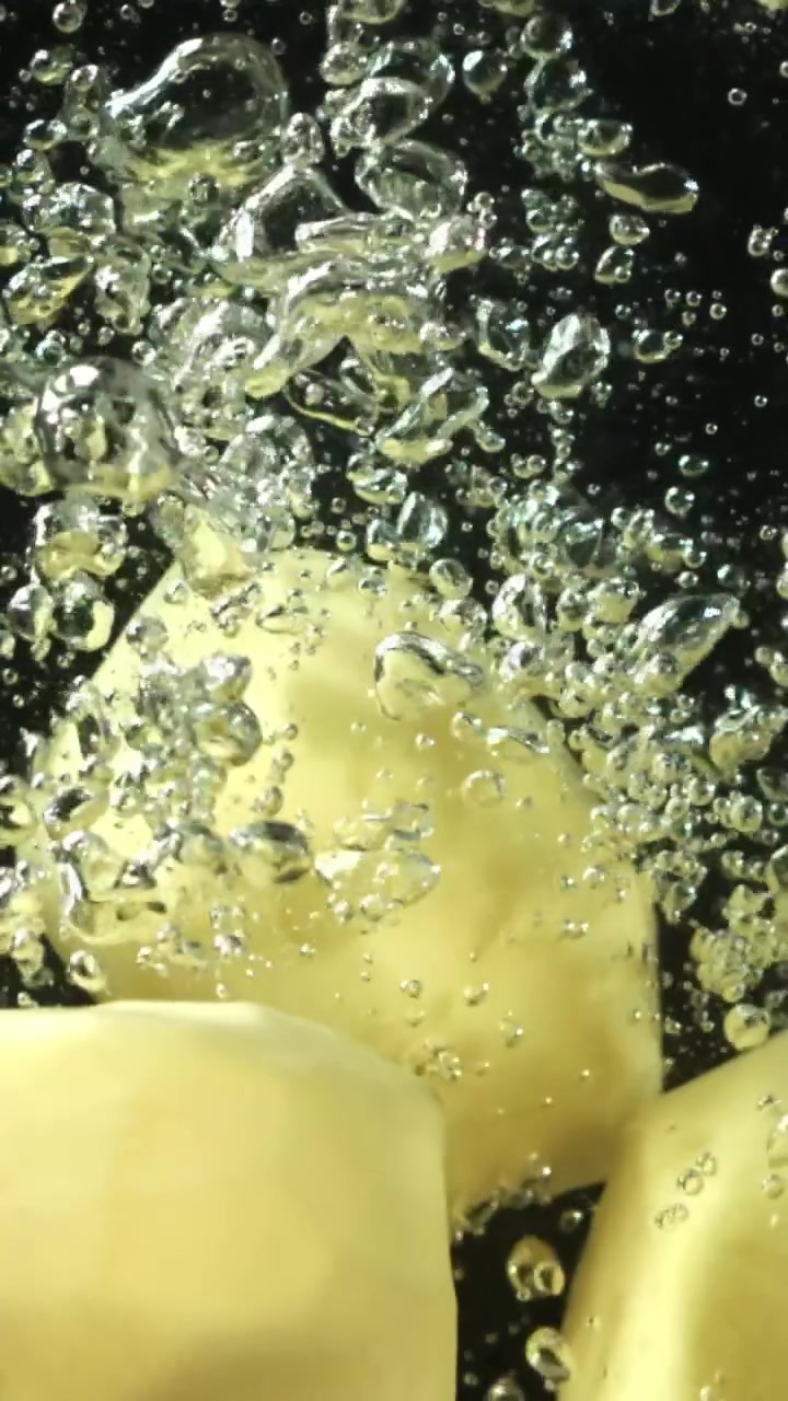 Patate pelate che cadono nell'acqua con bolle al rallentatore