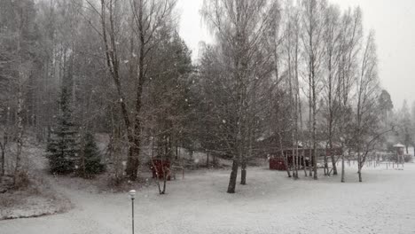 Grandes-Copos-De-Nieve-Cayendo-Lentamente-Frente-A-Un-Bosque-Con-Una-Casa-Roja-A-La-Derecha