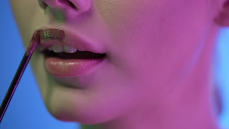 acercamiento extremo de una mujer joven y bonita aplicando brillo de labios brillante en sus hermosos labios rojos mientras se prepara para salir con amigos para una noche de club o una cita con luz de contraste púrpura en su cara