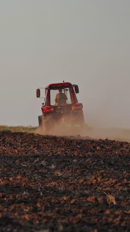 brown field background and a tractor plowing the soil. tractor cultivating the field, preparing land for sowing in the farmland. vertical video