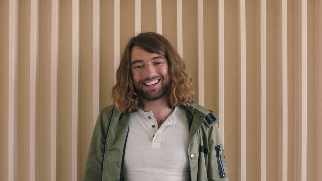 portrait of relaxed friendly young caucasian man with long hair laughing happy looking at camera cheerful male wooden background