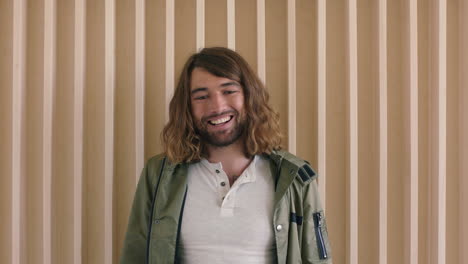 portrait of relaxed friendly young caucasian man with long hair laughing happy looking at camera cheerful male wooden background