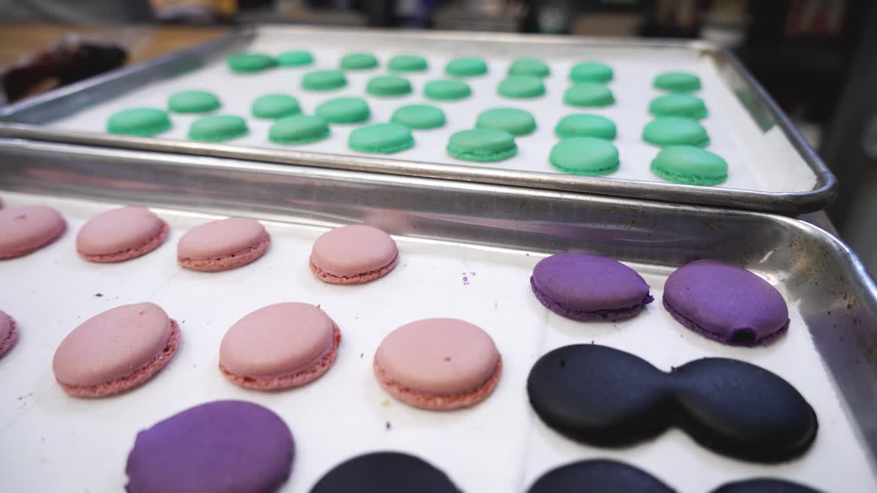 Colorful freshly baked french macarons fill trays in bakery, pink purple green cookie shells, close up 4K