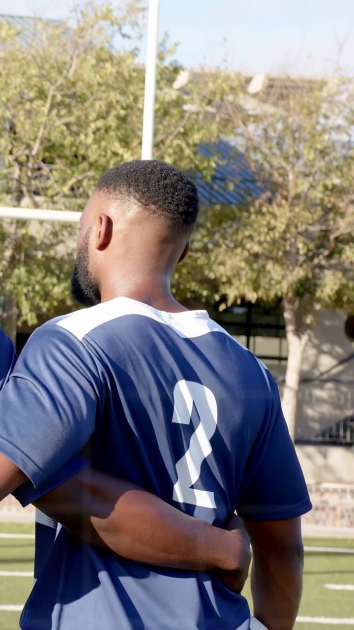 Vídeo vertical: Jogador de uniforme azul-marinho segurando a bola, companheiro de equipe abraçando, com sobreposição de interface do usuário surgindo durante a prática esportiva.