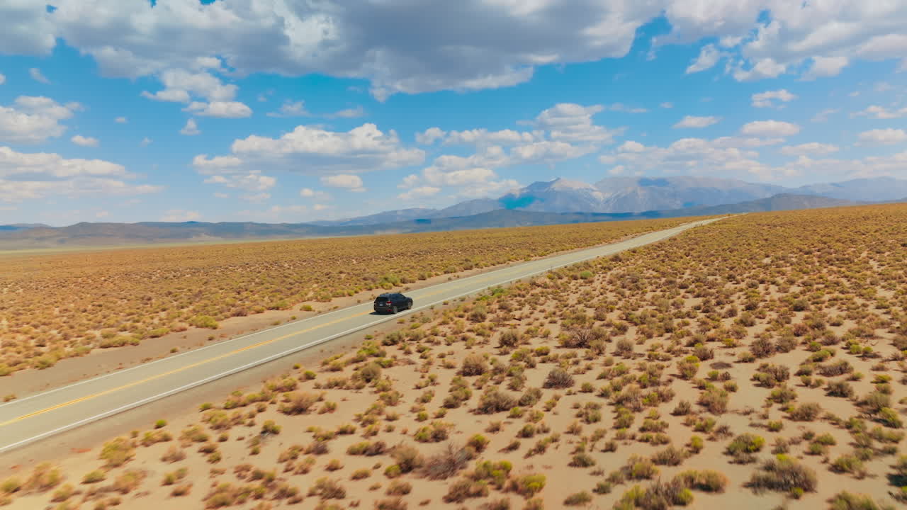 Catching up with a black car moving by the empty road through the desert. Beautiful blue sky with soft white clouds.