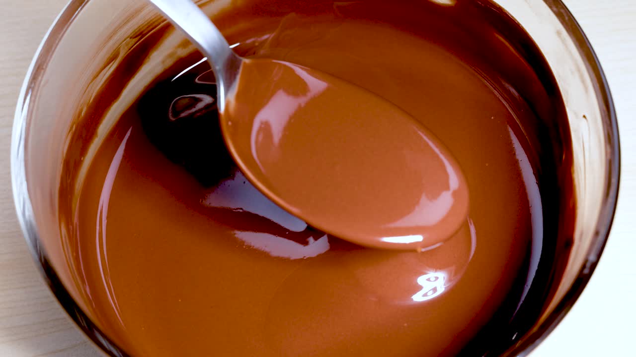 Cucchiaio che mescola cioccolato fuso e vellutato in una ciotola di vetro