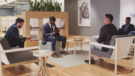 group of businessmen having informal discussion in seating area of modern open plan office