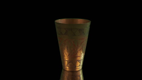 antique etched brass cup isolated on black background rotates