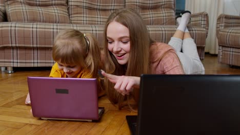 woman nanny and child girl studying together with computer laptop, while lying on warm floor at home