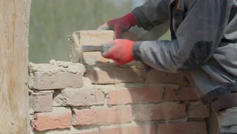 worker on deconstruction site cleans brick from mortar with hammer