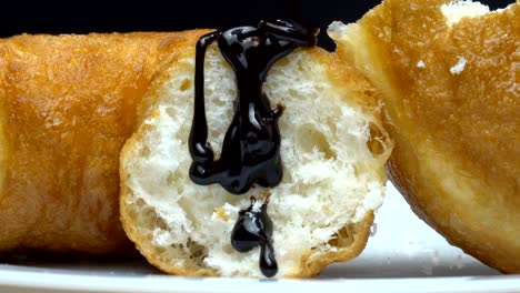 a piece of delicious sweet donut pouring by hot melted cocoa. camera zooms in.