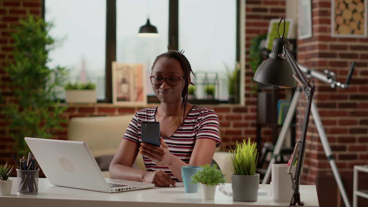 Donna che utilizza lo smartphone mentre lavora al laptop in ufficio