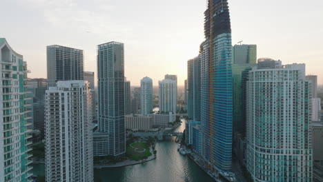 River-flowing-in-city-between-modern-high-rise-office-or-residential-skyscrapers.-View-against-bright-sky-at-dusk.-Miami,-USA