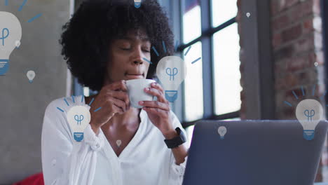 Animation-of-light-bulb-icons-over-african-american-businesswoman-using-laptop