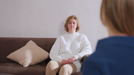 guest seated on brown sofa opposite therapist listening intently and nodding in response during therapy session pillow at side, neutral wall background and soft warm lighting in cozy counseling room