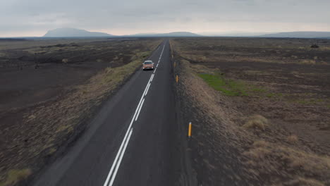 Drone-view-car-driving-along-ring-road-in-Iceland,-enjoying-exploring-wild-countryside.-Bird-eye-view-of-majestic-icelandic-highlands-with-car-speeding-motorway.-Commercial-insurance-concept