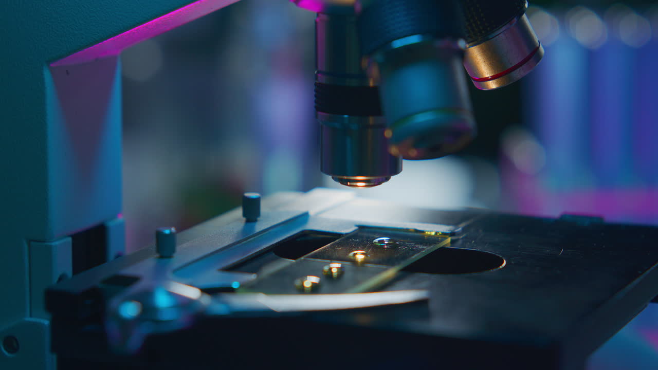 Microscope Lens Focusing on Slide under Neon Light in Laboratory