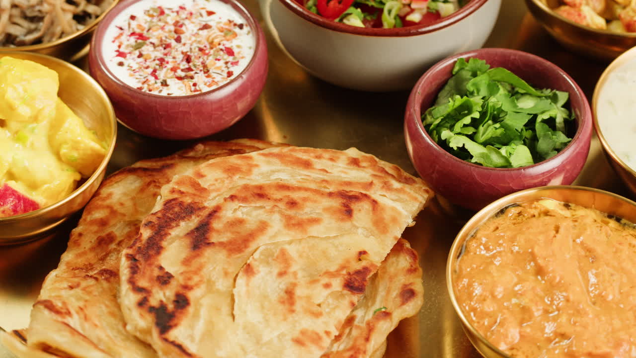 Assorted indian sri-lanka food set on wooden background. Dishes and appetisers of indeed cuisine, rice, lentils, paneer, samosa, spices, masala. Bowls and plates with indian food top view chicken. High quality 4k footage