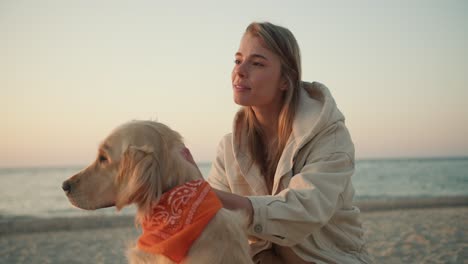 portrait of a young blonde girl who strokes her dog in the morning on the seashore. morning walk with a pet on the beach at sunrise