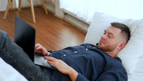 relaxed bearded guy lies on the floor on the pillow. man uses laptop working or for fun.