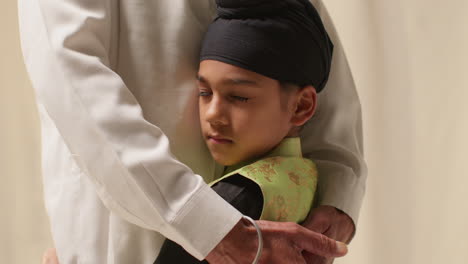 close up studio shot of young sikh boy with top knot turban hugging grandfather against plain background 3