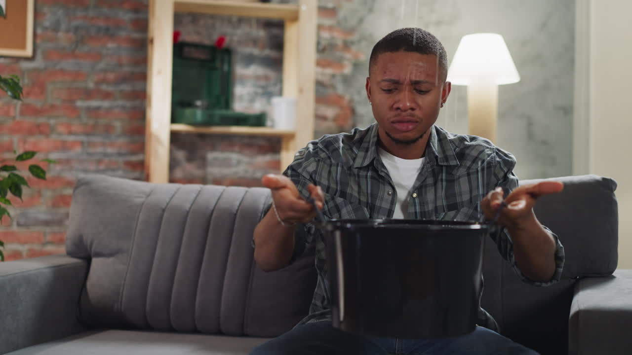 Black man collects water into basin during leakage in flat