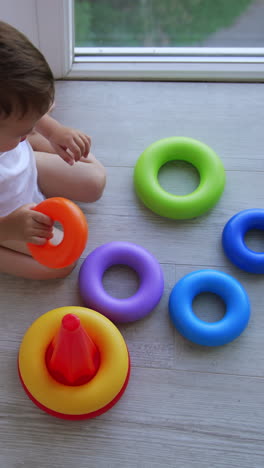 cute baby boy plays with toy pyramid. kid crawls by the floor picking up the necessary parts. top view. vertical video
