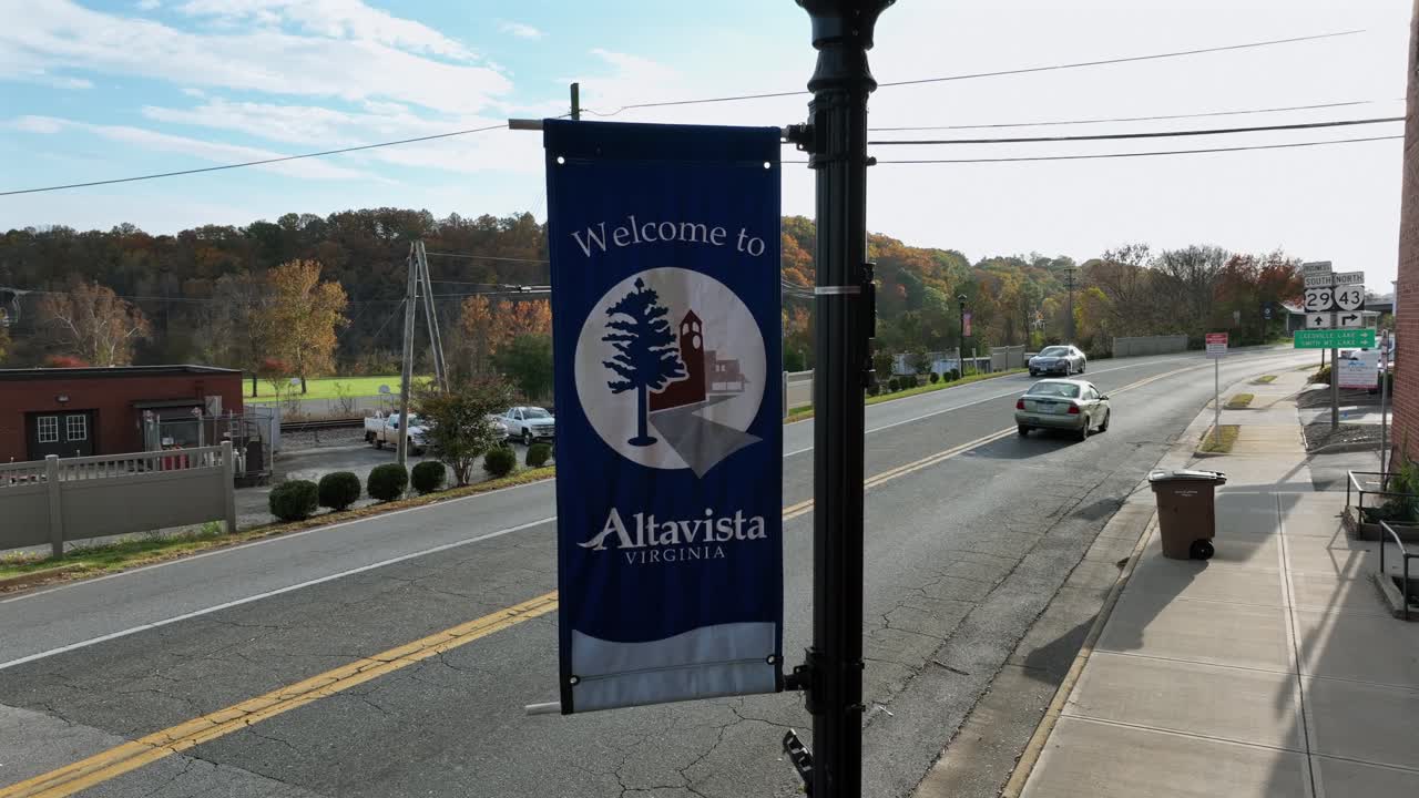 Welcome to Altavista, Virginia Flag on streetlamp of city. Driving cars on Street in historic town during autumn day. Aerial close up shot.