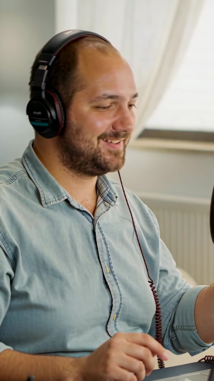 Vertical video: Preparing man in blue shirt raising headphones, leaning into mic to record at home