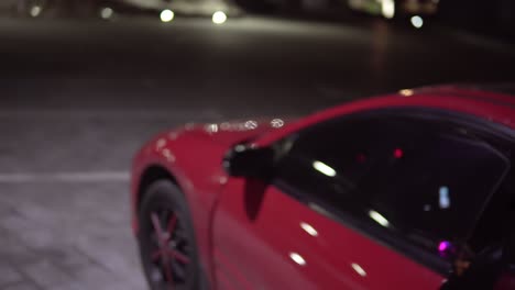 young man gets out of a red car at night at the parking. back view.