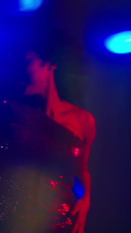 Vertical-Video-Of-Young-Woman-In-Nightclub-Bar-Or-Disco-Dancing-With-Sparkling-Lights-In-Background